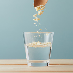 グラスに入った水に大豆パウダーをスプーンで振り入れている。