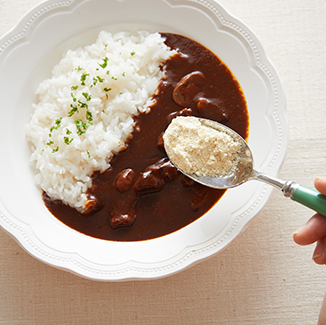 皿に盛られたカレーライスに大豆パウダーをスプーンでかけようとしているところ