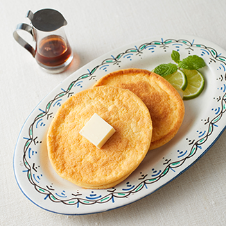 小麦粉の代わりに大豆パウダーで作ったパンケーキ2枚にバターひとかけら乗っている。そばにはメープルシロップのボトルがある。