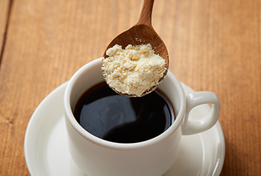 カップに入ったコーヒーにスプーンでダイズパウダーを注ごうとしている